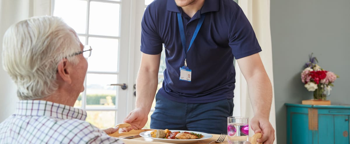 A care worker serving dinner to an older man