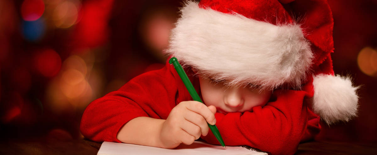 A child writing a Christmas list with a Santa hat on