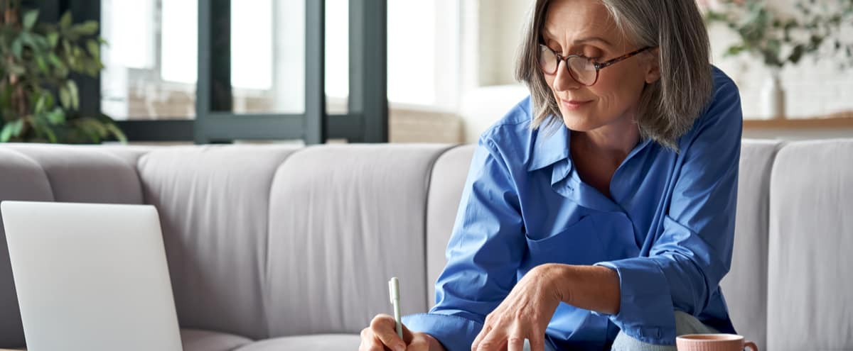 An older woman making notes from a laptop screen.