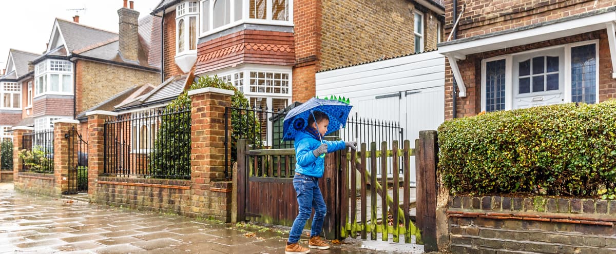 A boy with an umbrella opening a gate to a home.