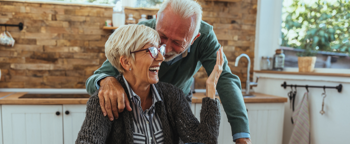 An older couple laughing together in their kitchen.