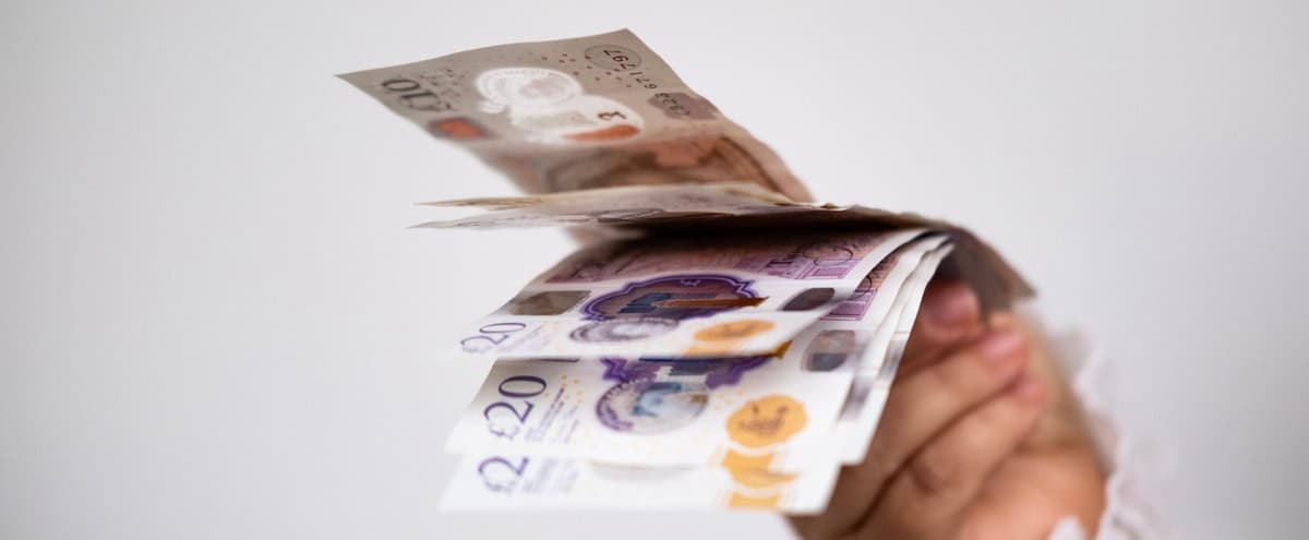 A hand holding UK bank notes.
